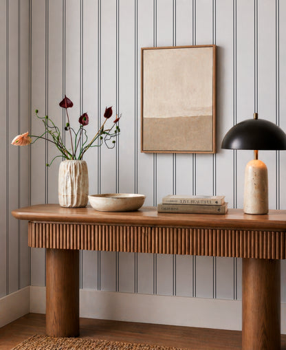 a wooden console table with a vase of flowers, a bowl, and a stack of books on it. The table is set against a striped wall, and there is a framed picture hanging on the wall.