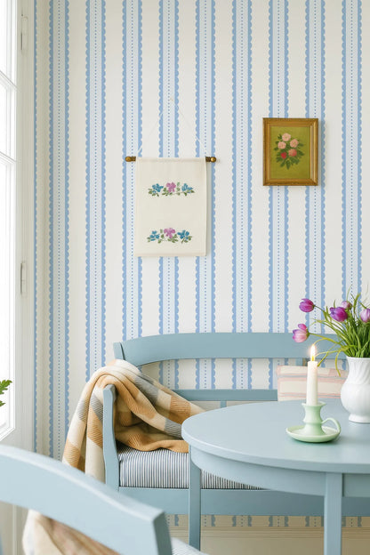 a cozy and charming living room with a blue and white striped wallpaper, a wooden bench, a small table with a vase of purple flowers, and a framed picture on the wall.