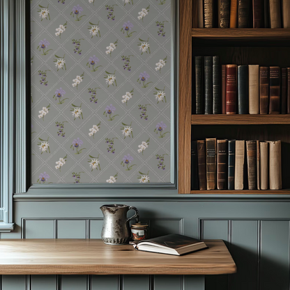 a cozy corner of a room with a wooden bookshelf filled with books, a metal pitcher, and a wooden table with a book and a candle.