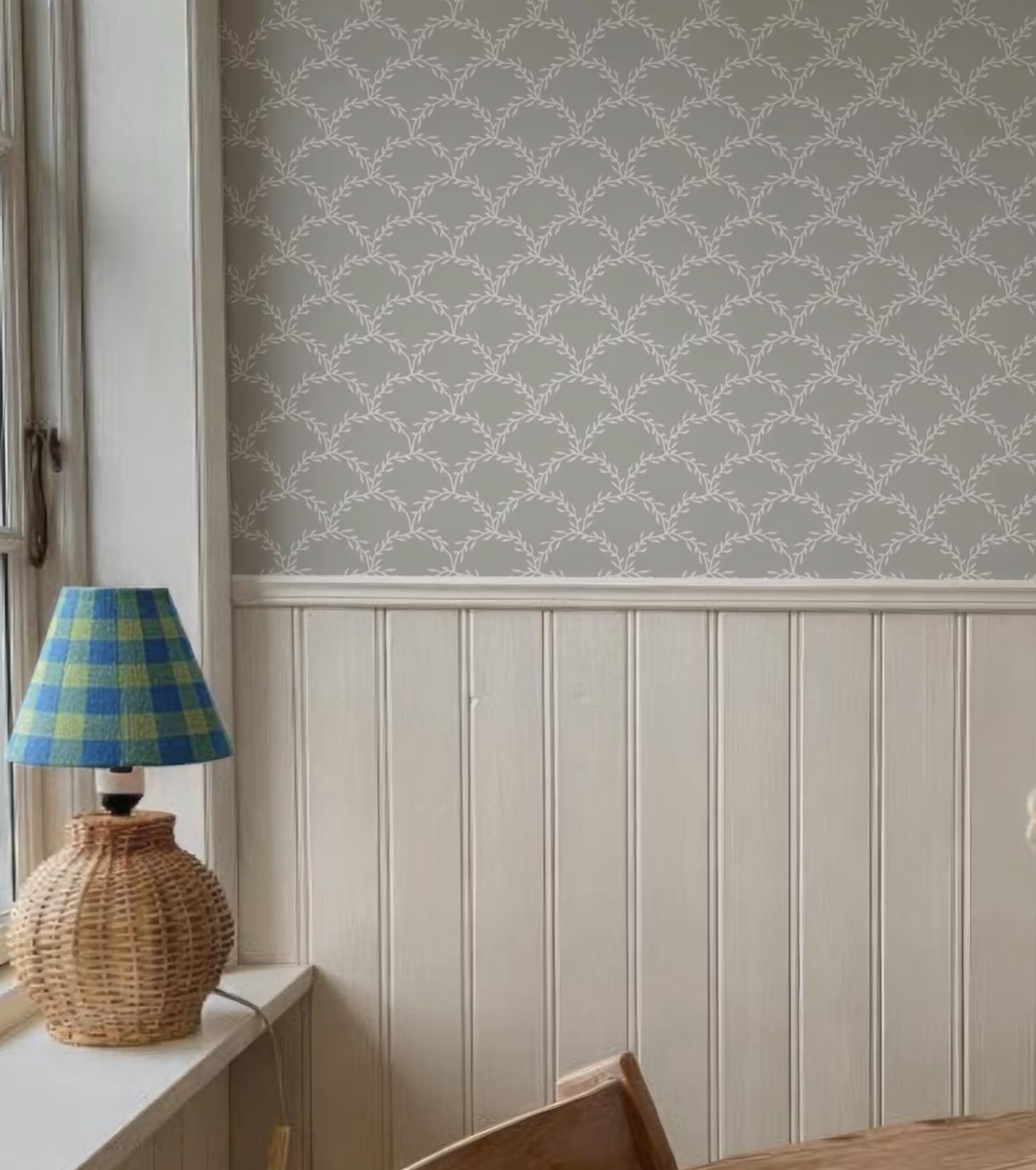 a wicker lamp with a blue and yellow checkered shade placed on a windowsill, next to a wall with a gray and white patterned wallpaper.