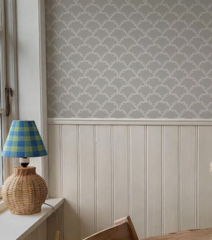 a wicker lamp with a blue and yellow checkered shade placed on a windowsill, next to a wall with a gray and white patterned wallpaper.