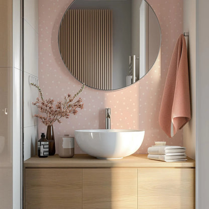 a bathroom with a white sink, a round mirror, and a wooden vanity. The bathroom has a pink and white color scheme, and there are some decorative elements such as a vase of flowers and a folded towel.