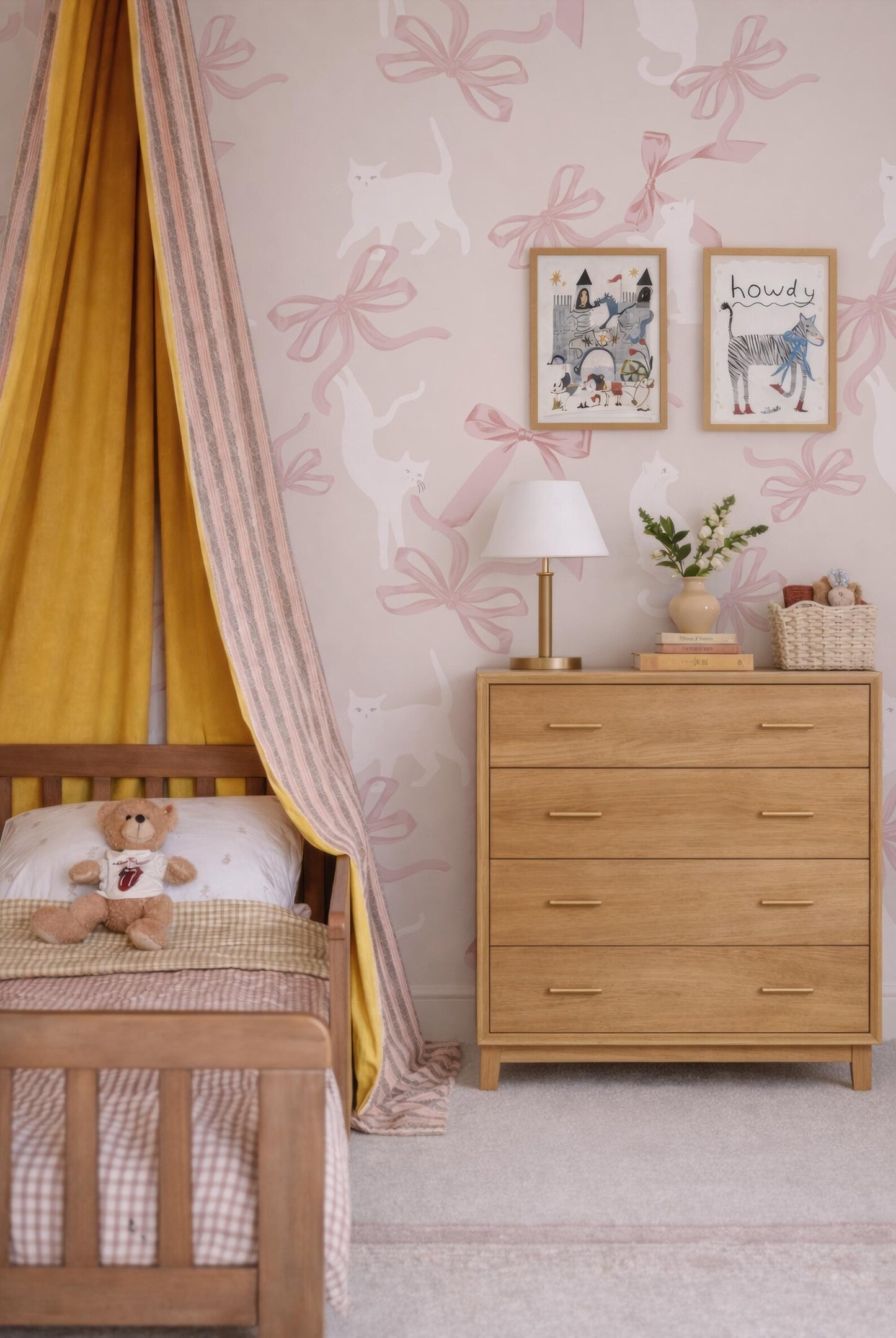 a cozy and charming bedroom scene, featuring a wooden dresser with a lamp, a teddy bear, and a framed picture on the wall. The walls are adorned with pink and white bows, and the overall color scheme is warm and inviting.