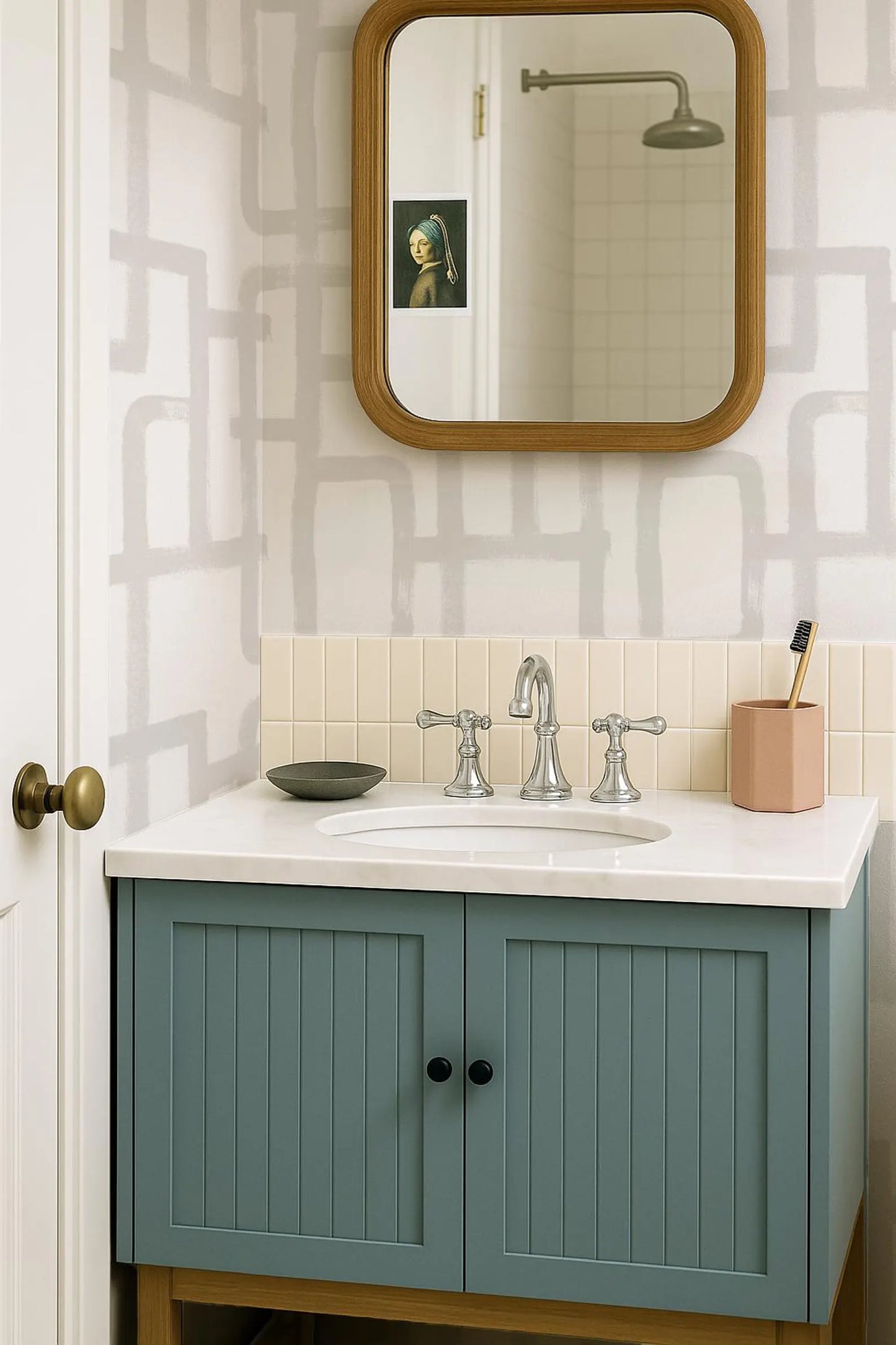 a bathroom with a blue cabinet, a white sink, and a mirror above it. The walls are covered in a patterned wallpaper, and there is a toothbrush holder on the counter.
