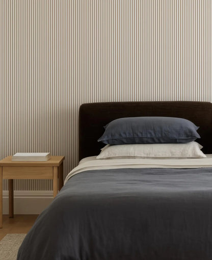 a neatly made bed with a dark brown headboard and a gray comforter. The bed is set against a striped wallpaper, creating a cozy and inviting atmosphere.