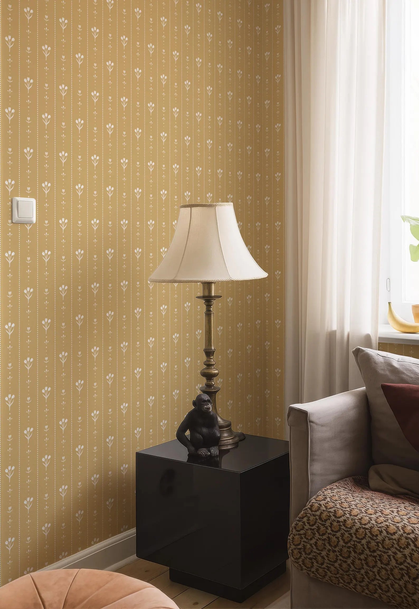 a cozy living room corner with a lamp, a black side table, and a patterned couch. The wall behind the furniture has a repeating pattern of white flowers, creating a warm and inviting atmosphere.