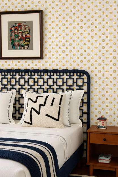 a bedroom with a bed, a nightstand, and a framed picture on the wall. The bed has a black headboard and white pillows, and the wall is covered in yellow and white patterned wallpaper.