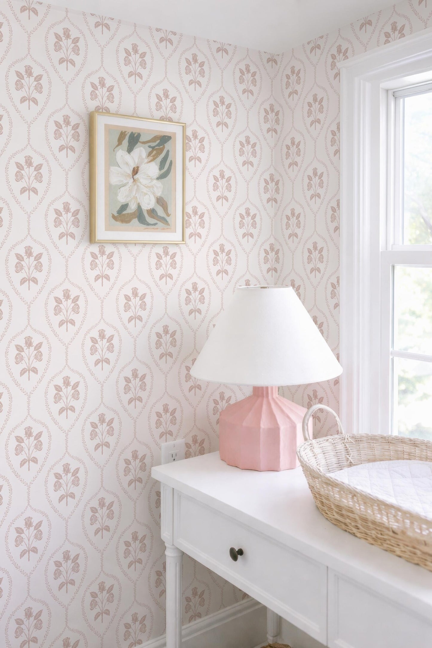 a white dresser with a pink lamp, a white basket, and a framed picture on the wall.