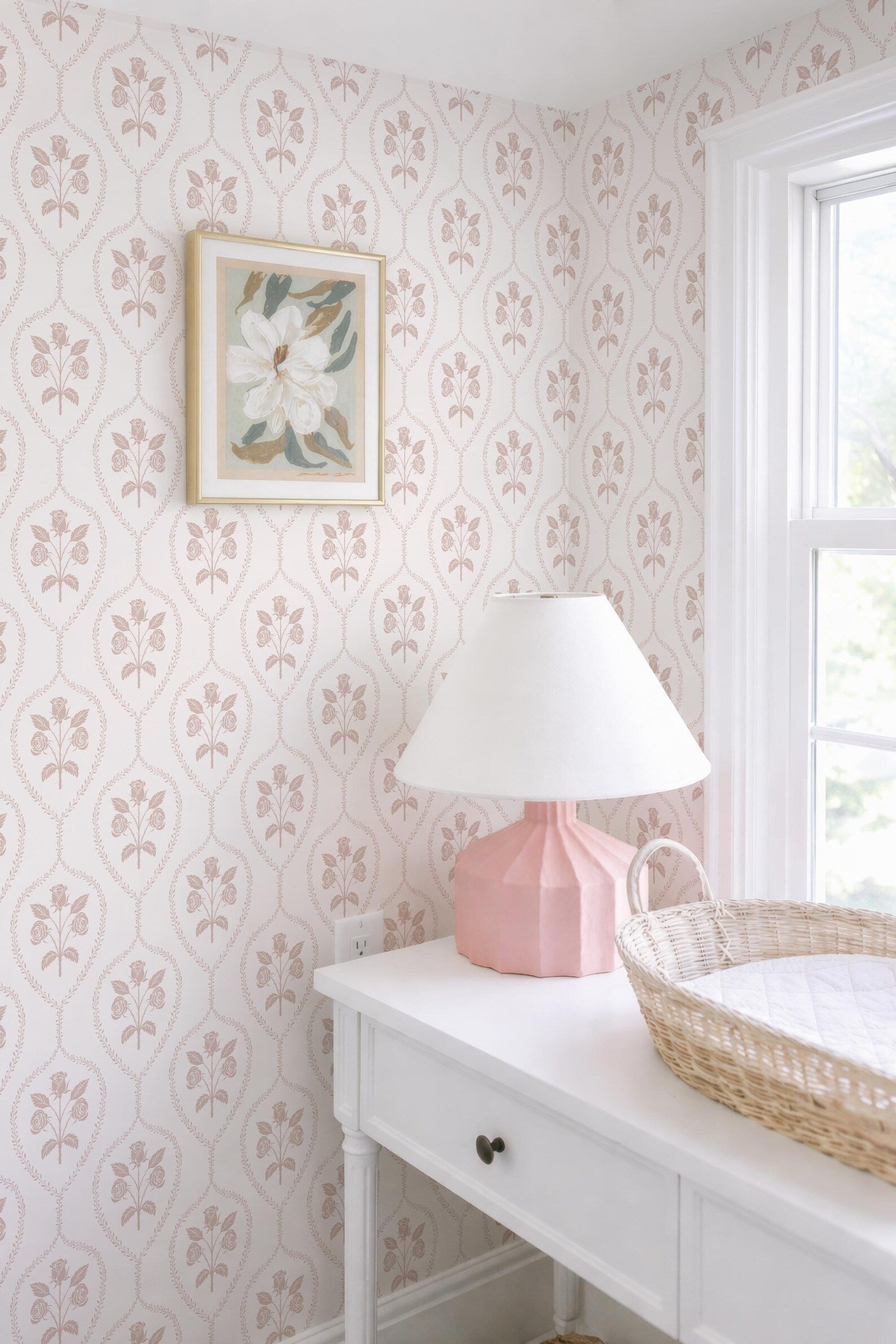 a white dresser with a pink lamp, a white basket, and a framed picture on the wall.