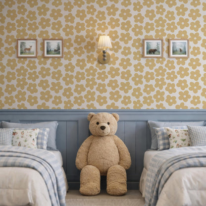 a cozy bedroom with a large teddy bear sitting between two beds. The walls are adorned with yellow and white floral wallpaper, and there are two framed pictures hanging above the beds. The room has a warm and inviting atmosphere, with the teddy bear adding a touch of comfort and playfulness to the space.
