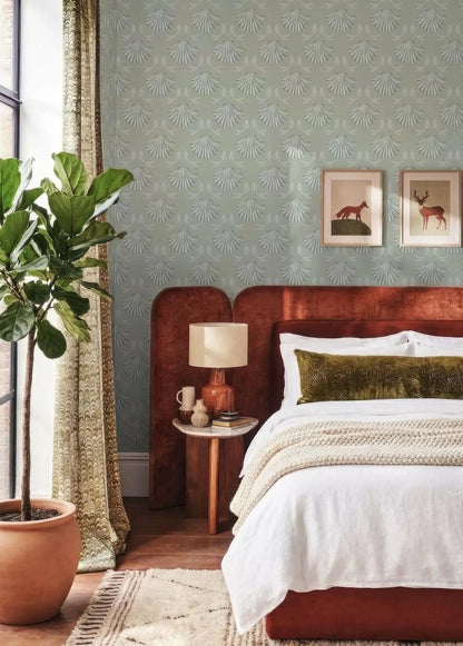 a cozy bedroom with a large bed, a wooden nightstand, and a potted plant. The walls are covered in a patterned wallpaper, and there are two framed pictures on the wall. The room has a warm and inviting atmosphere, with a mix of natural and modern elements.