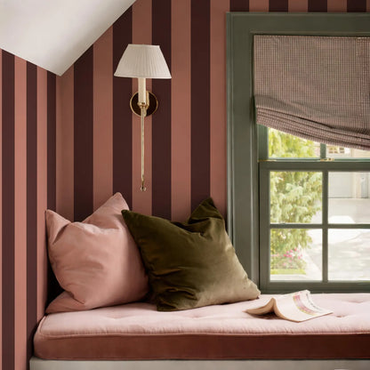 a cozy corner of a room with a window, a lamp, and a comfortable bed with pillows.