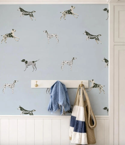 a wall with a pattern of black and white spotted dogs, and there are two coats hanging on a rack below the wall.