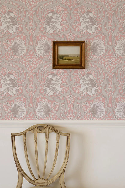 a wooden chair with a floral patterned wall behind it, and a framed landscape painting hanging on the wall.