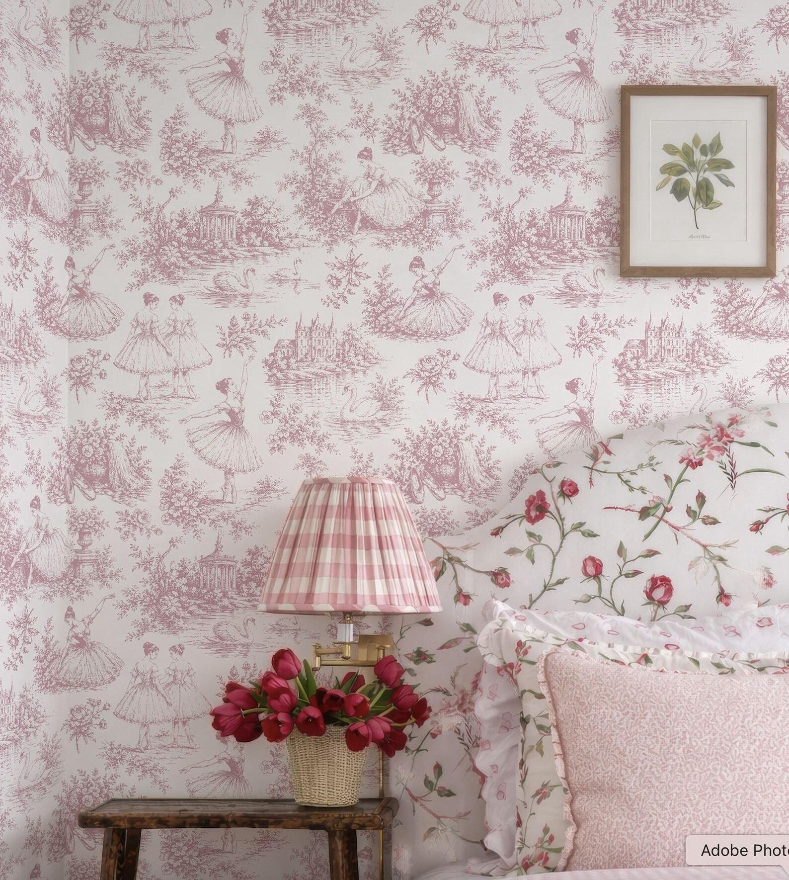 a bedroom with a pink and white floral wallpaper, a wooden nightstand with a lamp and a vase of red flowers, and a framed picture on the wall.