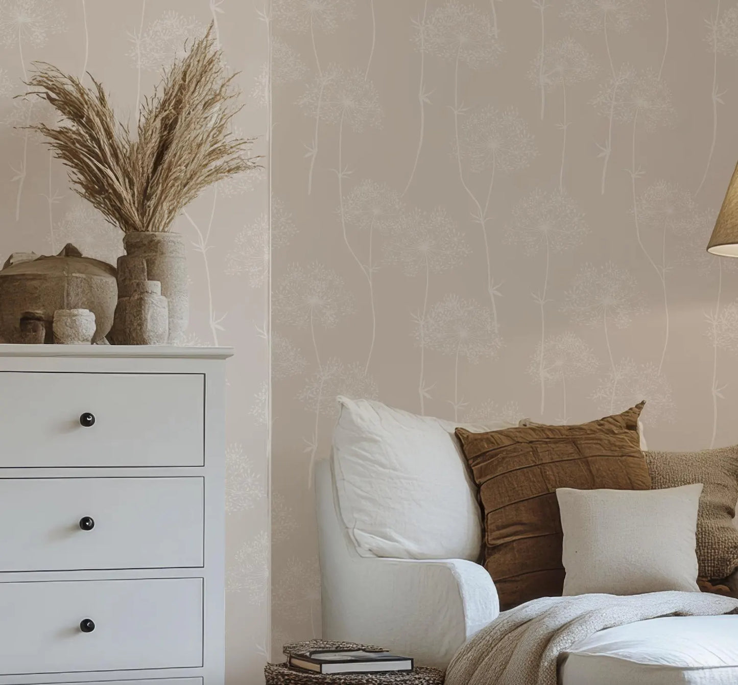 a cozy living room with a white sofa adorned with brown throw pillows, a white dresser, and a vase of dried flowers on top of the dresser.