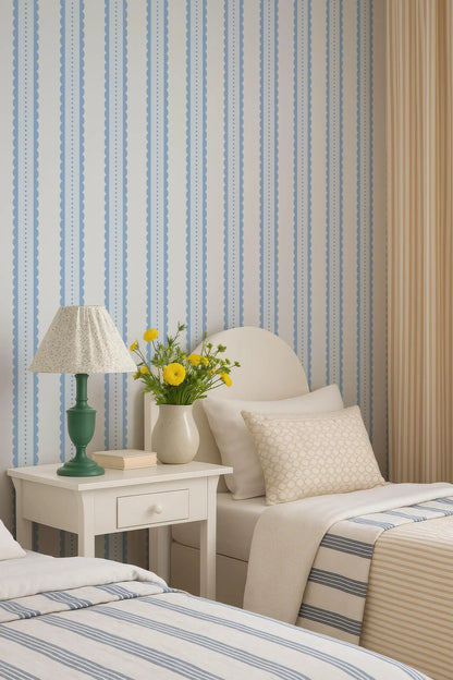 a cozy bedroom with a white bed, a nightstand with a lamp and a vase of yellow flowers, and striped wallpaper.