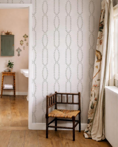 a cozy corner of a room with a wooden chair, a patterned curtain, and a white wall with a repeating leaf design.