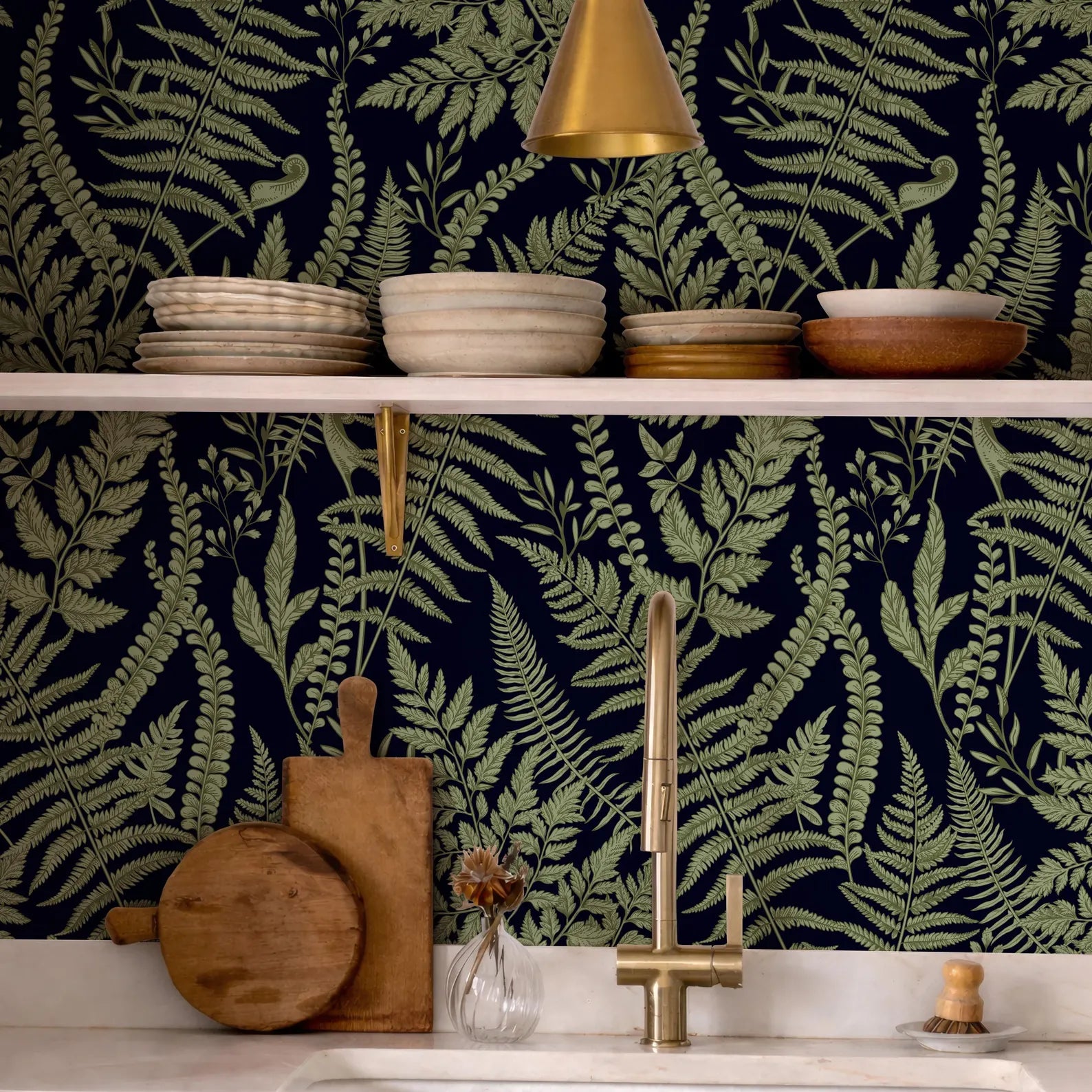 a kitchen counter with a variety of kitchen items, including a wooden cutting board, a vase with flowers, and a sink with a gold faucet. The counter is set against a dark green wall with a fern-like pattern, creating a cohesive and visually appealing design.