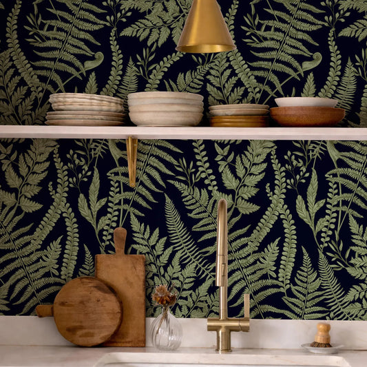 a kitchen counter with a variety of kitchen items, including a wooden cutting board, a vase with flowers, and a sink with a gold faucet. The counter is set against a dark green wall with a fern-like pattern, creating a cohesive and visually appealing design.