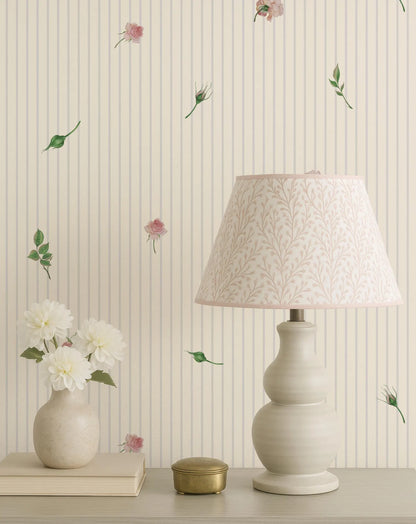 a table with a lamp, a vase with white flowers, and a book. The lamp has a white shade with a floral pattern.