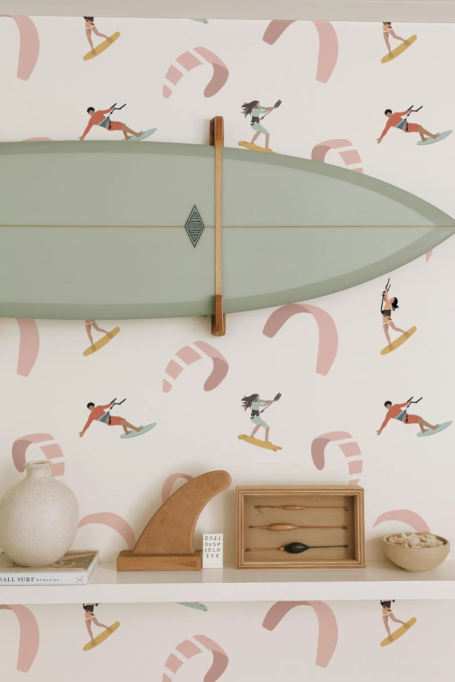 a wall with a surfboard mounted on it, along with various decorative items such as a wooden surfboard holder, a wooden sculpture, and a framed picture of a surfer. The wall also has a pattern of surfers and kites, creating a beach-themed atmosphere.