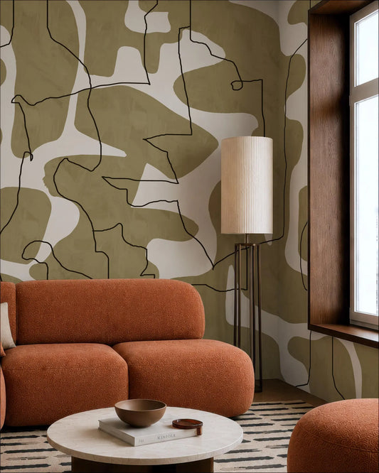 a modern living room with a large abstract wall mural in shades of green and brown. The room is furnished with a large orange sofa and a round coffee table. A floor lamp is positioned next to the sofa, and a window is visible on the right side of the room.