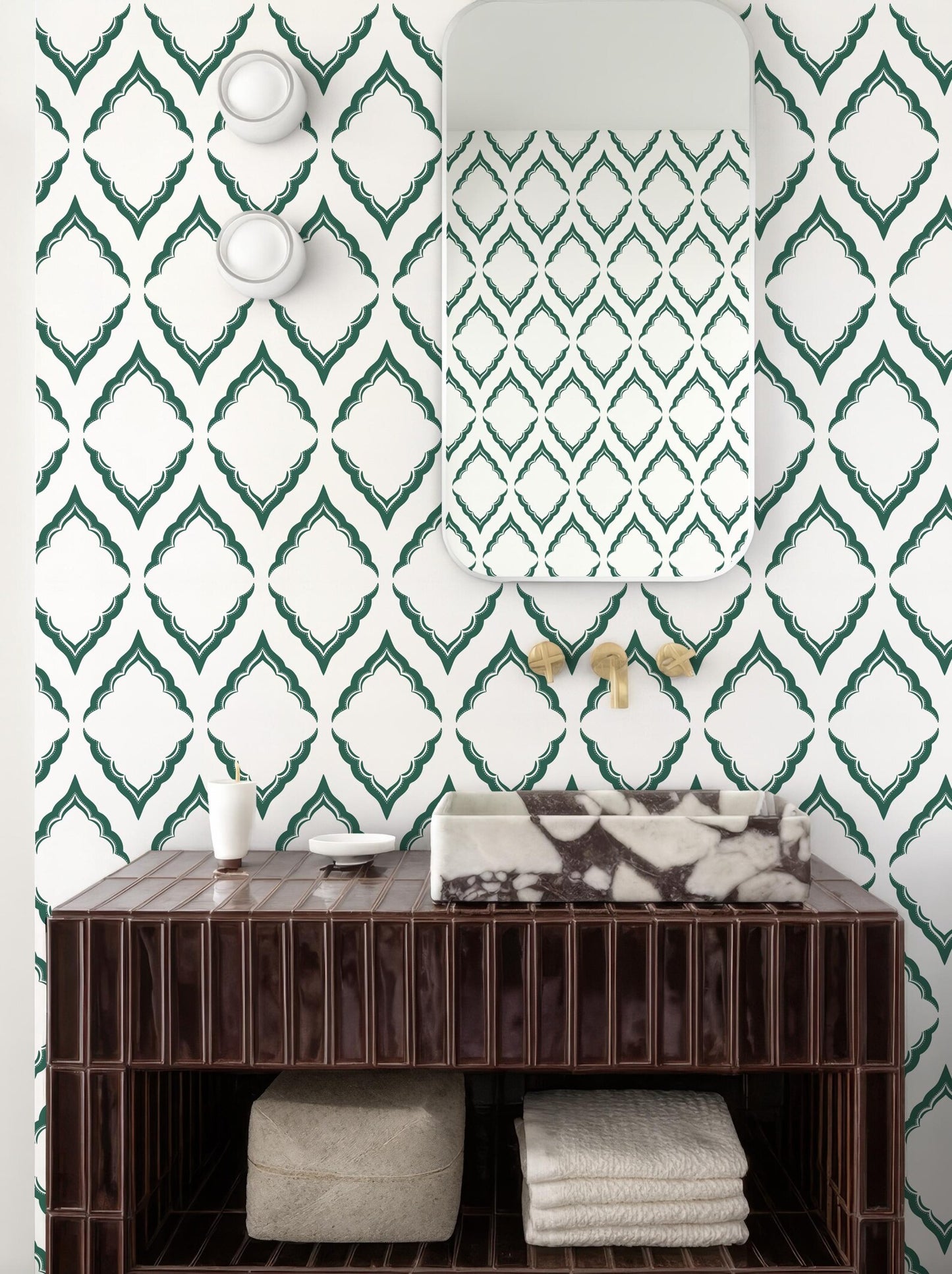 a bathroom with a brown wooden vanity, a marble-topped sink, and a mirror above it. The walls are covered in a patterned wallpaper with green diamond shapes. There are also two white light fixtures on the wall.
