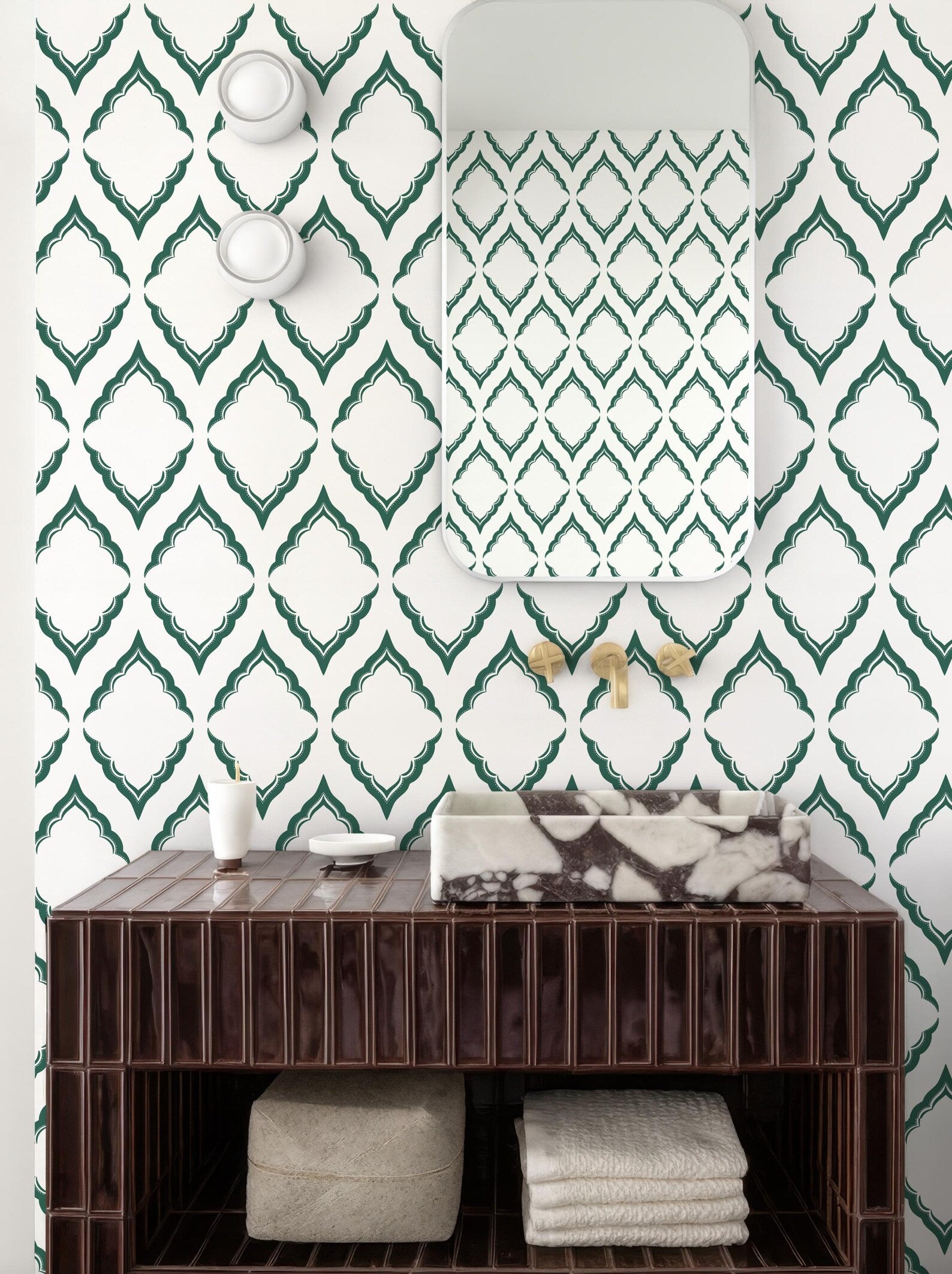 a bathroom with a brown wooden vanity, a marble-topped sink, and a mirror above it. The walls are covered in a patterned wallpaper with green diamond shapes. There are also two white light fixtures on the wall.