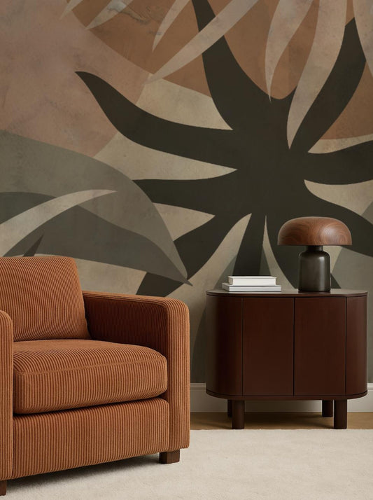 a living room with a brown armchair and a wooden side table with a lamp. The wall behind the furniture has a large abstract design in shades of brown and black.