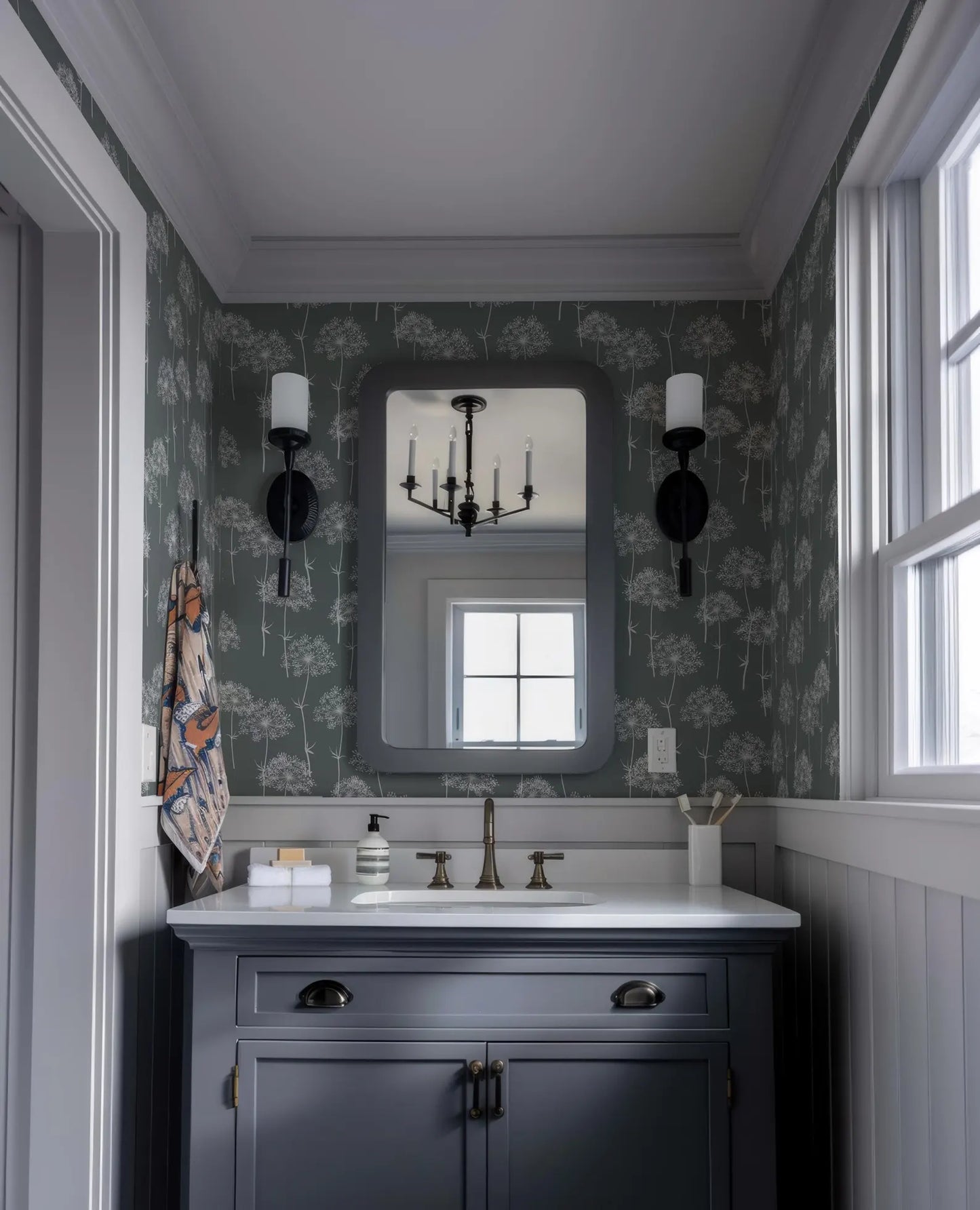 a bathroom with a white sink, a mirror, and a chandelier above it. The walls are covered in a patterned wallpaper, and there are two wall sconces on either side of the mirror. The overall color scheme of the bathroom is predominantly gray and white.