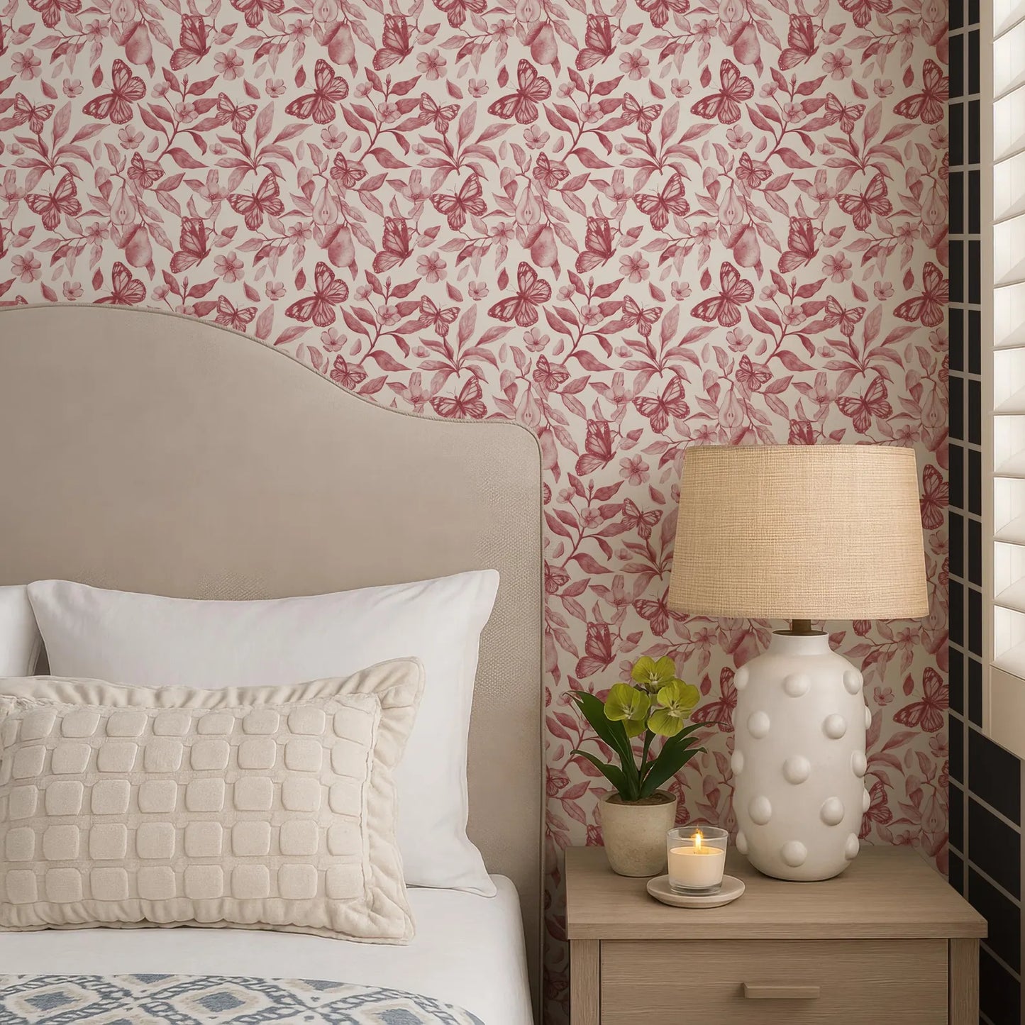 a cozy bedroom scene with a bed, a nightstand, and a lamp. The bed has a beige headboard and white pillows, and the nightstand has a white lamp with a beige shade. The wall behind the bed is decorated with a floral wallpaper featuring red and pink butterflies.