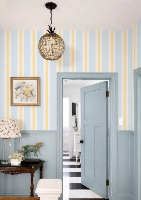 a room with a blue door, a chandelier, and a painting on the wall. The door is open, revealing a hallway beyond.