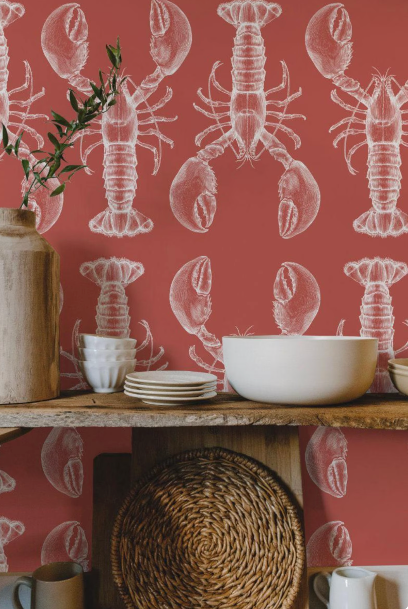 a kitchen shelf with various items, including a bowl, plates, a vase, and a wicker basket. The wall behind the shelf has a repeating pattern of white lobster illustrations, creating a coastal or nautical theme.
