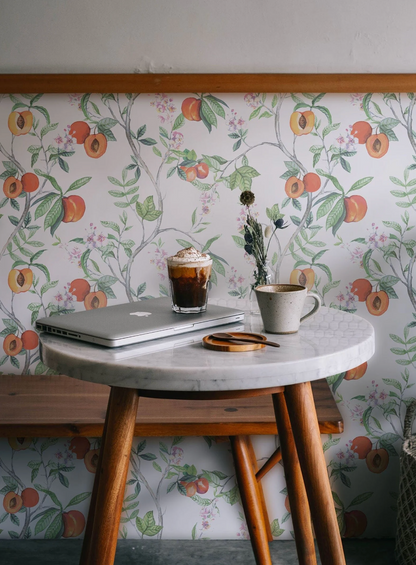 a cozy and inviting scene with a round wooden table, a laptop, a cup of coffee, and a vase of flowers. The table is set against a wall with a floral wallpaper, creating a warm and welcoming atmosphere.